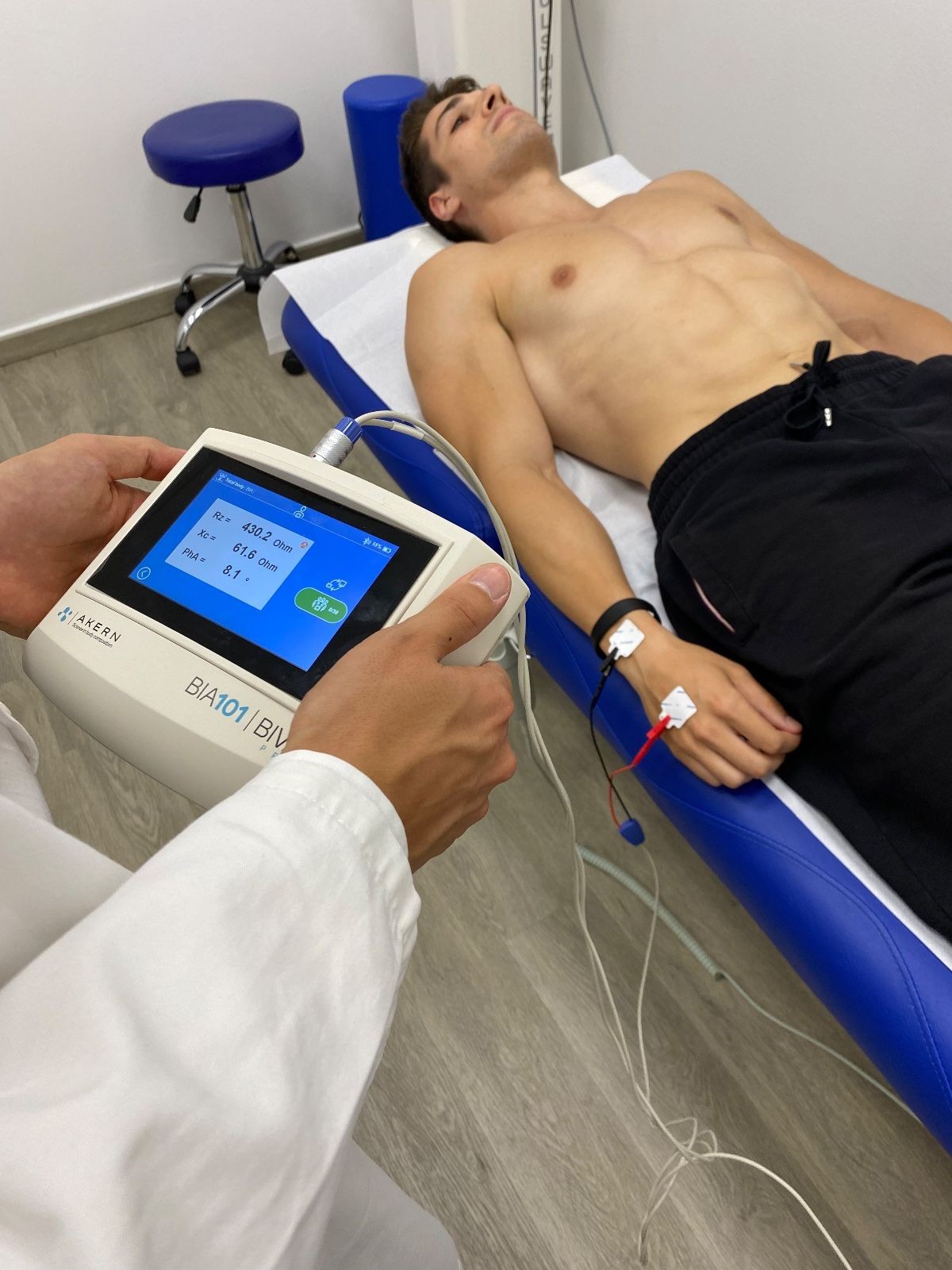 Person conducting a BIA test on a man lying on an examination table in a clinic.